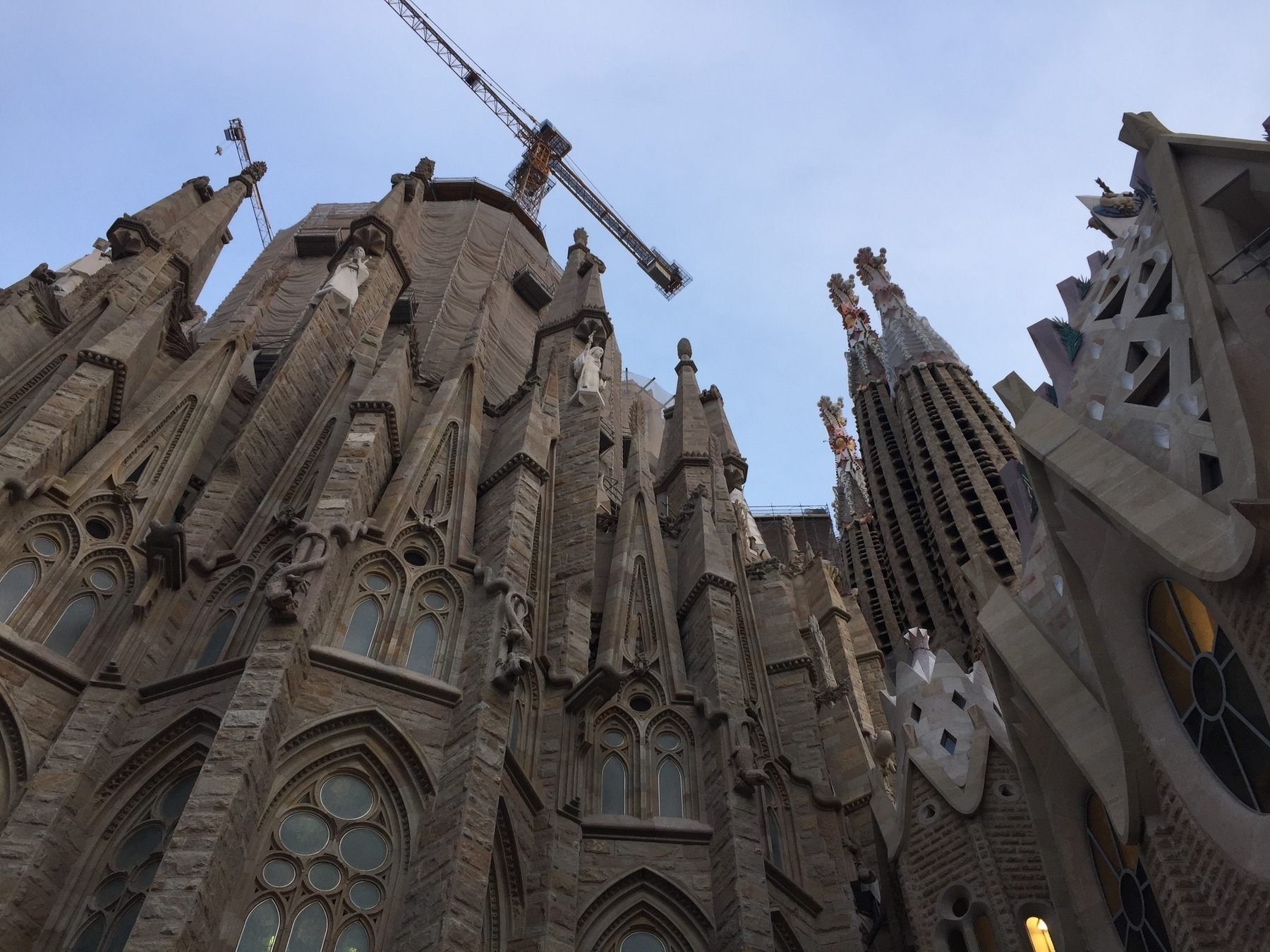 A view of the intricately designed exterior of the Sagrada Família in Barcelona, featuring towering spires and cranes against a clear sky.