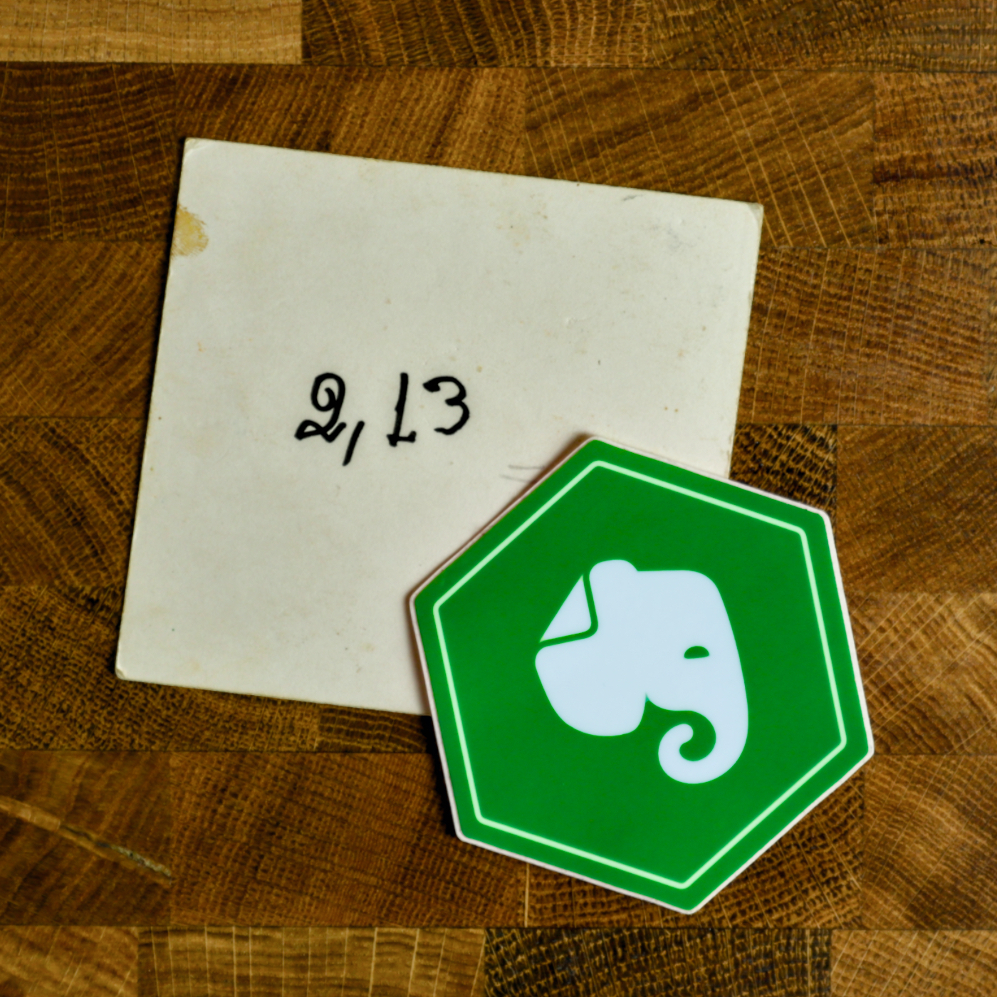 Auto-generated description: A square piece of paper with the handwritten text 21,3 lies beside a green hexagonal sticker featuring a white elephant logo.