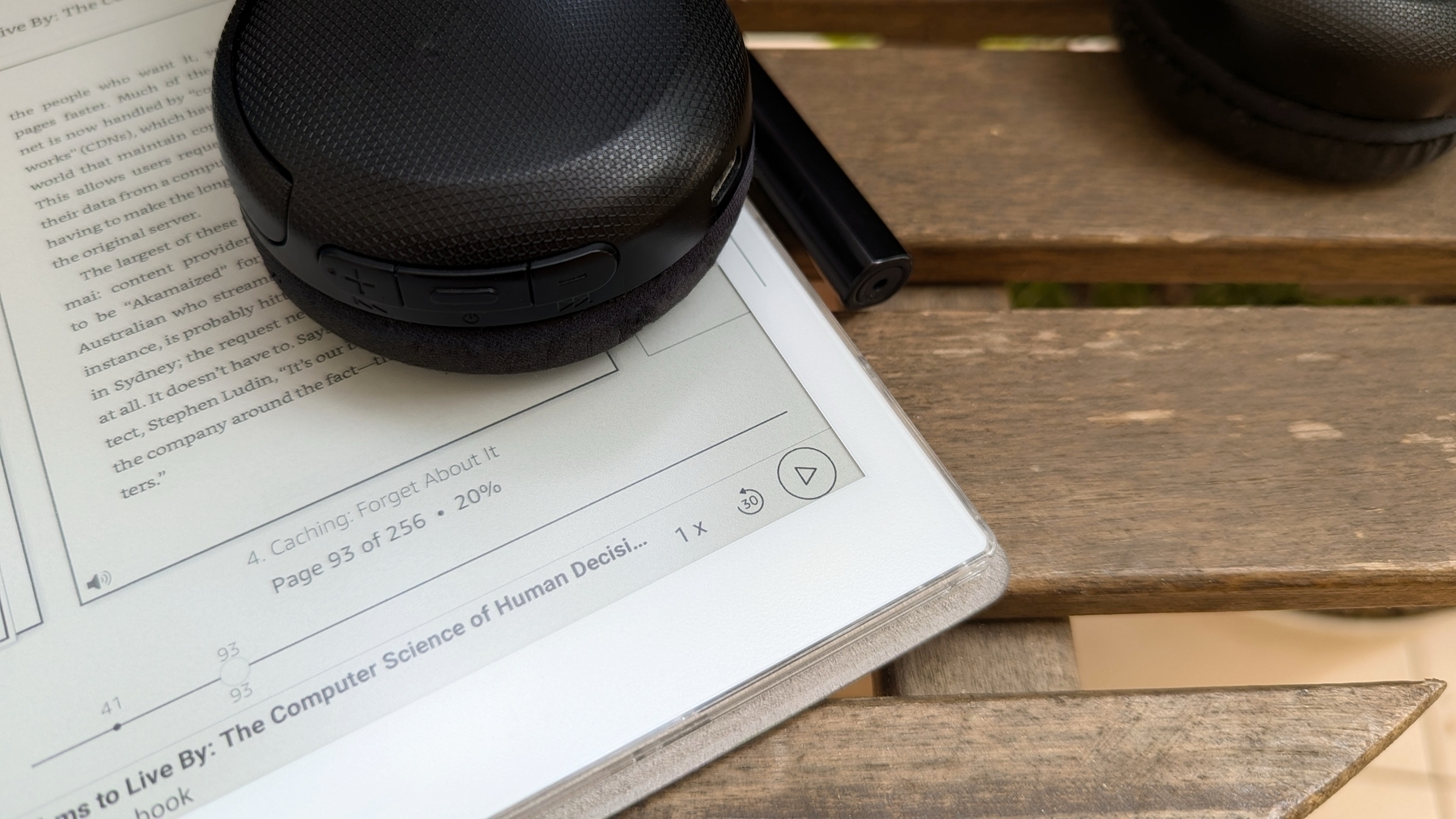 A pair of black headphones and a pen rest on an open Supernote Nomad displaying a book, placed on a wooden surface.