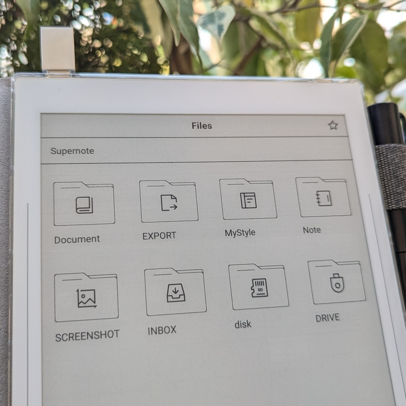 A Supernote Nomad A6X2 displaying various file management icons under categories like Document, Export, Note, and Drive, against a background of green leaves.