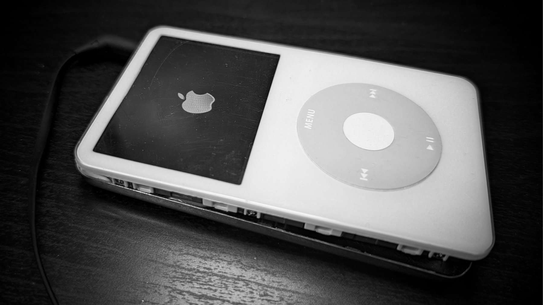 An opened iPod 5 (iPod Video) is connected to a cable and placed on a dark wooden surface.